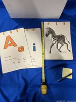 Three sample cards shown (A, i, Z) beside tape measure and pen for scale