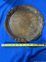 Top view showing carved pineapple leaf border and sunburst center with tape measure for scale
