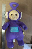 Front view of purple Tinky Winky plush doll beside ruler showing height