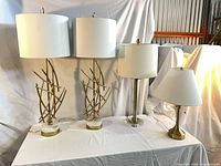 Four lamps displayed: two tall abstract rod marble base lamps, one clear acrylic/brass column lamp, one brass candlestick lamp