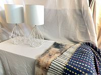 two white wireframe lamps beside folded textiles