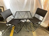 full view of glass-top table and two wicker folding chairs