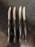 Four Cutco serrated steak knives aligned on dark surface