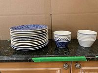 Stack of 12 plates and two stacks of assorted patterned bowls on countertop