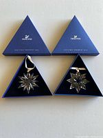 Both Swarovski ornaments displayed in open blue triangular boxes showing crystal stars and ribbons