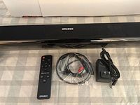 Top view of Sakobs sound bar with accessories laid out: remote, audio cable, power adapter