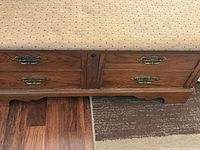 Front lower view showing wood exterior, faux drawers, brass pulls, portion of cushion