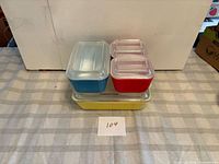 Stacked view of blue, red, and yellow Pyrex refrigerator dishes with lids
