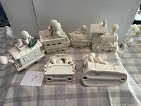 Six Snowbabies figurines arranged on table: four train pieces, Puppet Theater, log sled