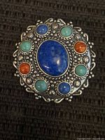 Front view of sterling pendant brooch showing lapis center, eight surrounding turquoise and coral cabochons