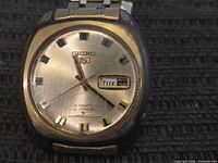Front view of Seiko watch showing dial, logo, day-date window, wear on crystal