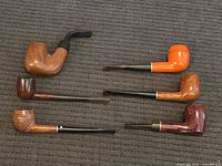 All six pipes laid out on dark fabric, showing overall styles and finishes