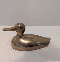 Side view of brass duck figurine showing polished surface and size perspective