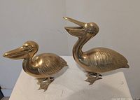 Two brass pelican figurines on tabletop showing different beak positions and detailing