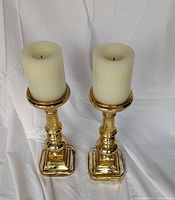 Two gold-coloured glass candle holders with pillar candles for scale on white backdrop