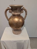 Front view of gold painted double-handled clay vase on stand