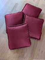 Four rusty red square cushions with ruffle trim on wood floor