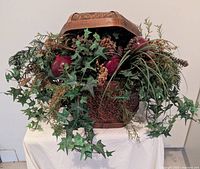 Front view of wicker basket with lid open showing artificial greenery, pinecones and faux pomegranates