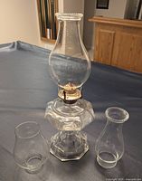 Front view of clear glass hurricane lamp with fitted chimney and two spare chimneys