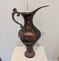 Full view of metal decorative pitcher showing handle, spout, pedestal base