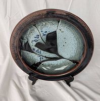 Front view of glazed pottery plate on black stand