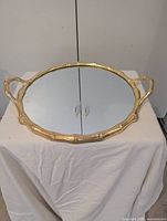 Round mirror tray with gold bamboo-style frame and handles, shown on draped surface
