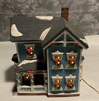 Front angled view showing blue ceramic house, wreath-decorated windows, attached white power cord