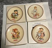 Four Hummel plates out of boxes showing motifs and year marks 1985 1986 1993 1994