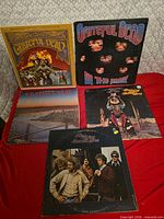Five vinyl album covers laid out on red cloth