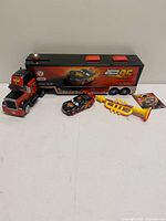 All four items together: transporter with trailer, Lightning McQueen car, trumpet, booklet