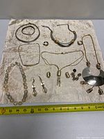 All twelve jewelry items laid out on cloth with tape for scale