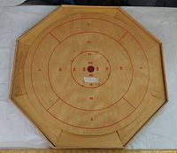 Full view crokinole board showing scoring rings, numbers, centre hole and one red disc