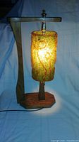 Full view of illuminated lamp showing wood frame, fiberglass shade, cord
