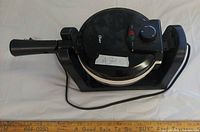 Closed waffle maker showing brand label, control dial, handle, attached cord