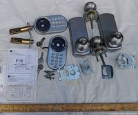 All components for both electronic door locks laid out including keypads, knobs, latch assemblies, strike plates, screws, keys and instructions