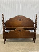 Front view of footboard showing wood finish, turned posts, carved panel