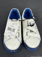 Top view of both sneakers showing white uppers, blue lining, velcro straps, and attached retail tag
