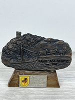 Front view of metal plaque on wood base showing relief scene and badges