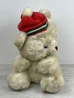 Side view of off-white teddy bear wearing red knit hat