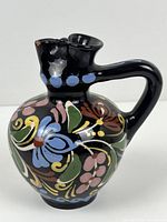 Front view of black glazed ceramic mini ewer vase with multicolour floral painting
