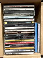 Full stack of approximately 23 CD jewel cases inside box, spines visible for artist and title identification