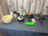 Full lot overview showing popcorn bowl, mugs, waffle maker, frying pans, glass lid, silicone container