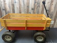 Full side view showing red metal tub, wooden slats, pull handle and pneumatic tires