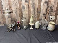 Entire lot lined up: two glass dispensers, packaged wine charms, ceramic bottle and jar, glass canister, ceramic vase