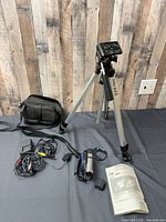 Tripod, carrying bag, cables, battery, manual grouped on surface