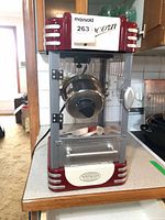 Front view of Nostalgia Electrics red/white popcorn maker showing cabinet, door and control panel