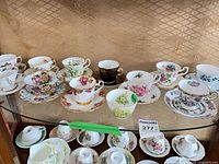 Shelf holding approximately 12 floral bone-china teacup and saucer pairs from Aynsley, Royal Albert and others