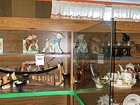 Wide shot of shelf with figurines, scale, amber glass and porcelain inside cabinet