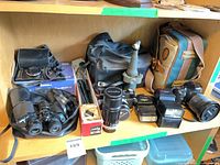 Shelf view of entire lot: binoculars, cameras, telescope, flashes, bags