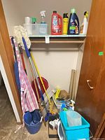 Full view of closet with mops, broom, buckets, dustpan, apron and shelf of cleaners